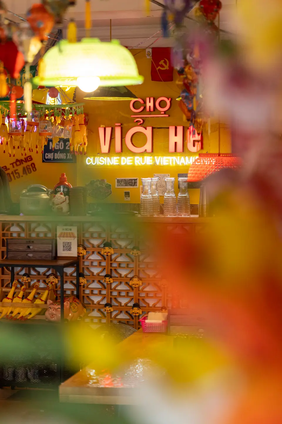 Enseigne néon rouge « CHỢ VỈA HÈ · Cuisine de rue vietnamienne » sur un mur jaune vif.