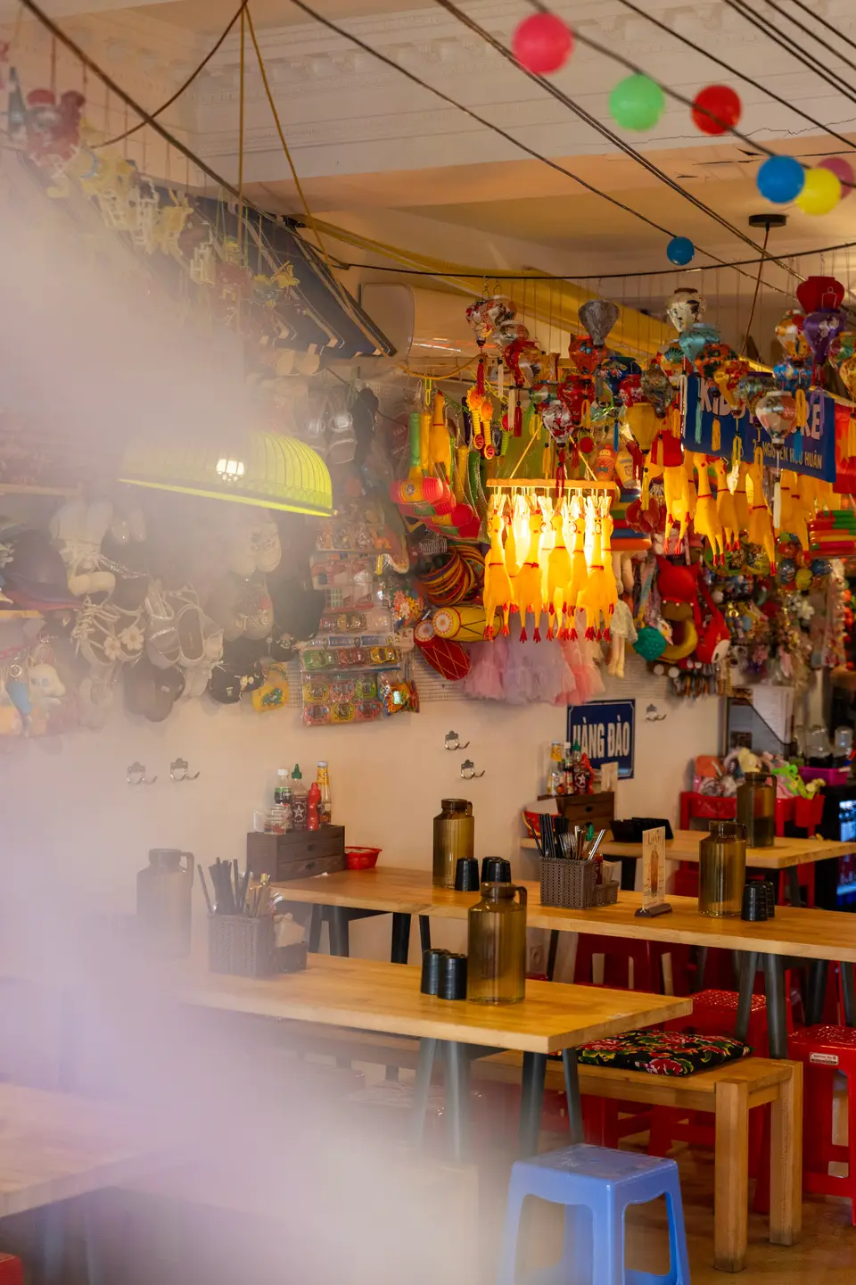 La salle façon marché : tables en bois, lampions et jouets suspendus au plafond.