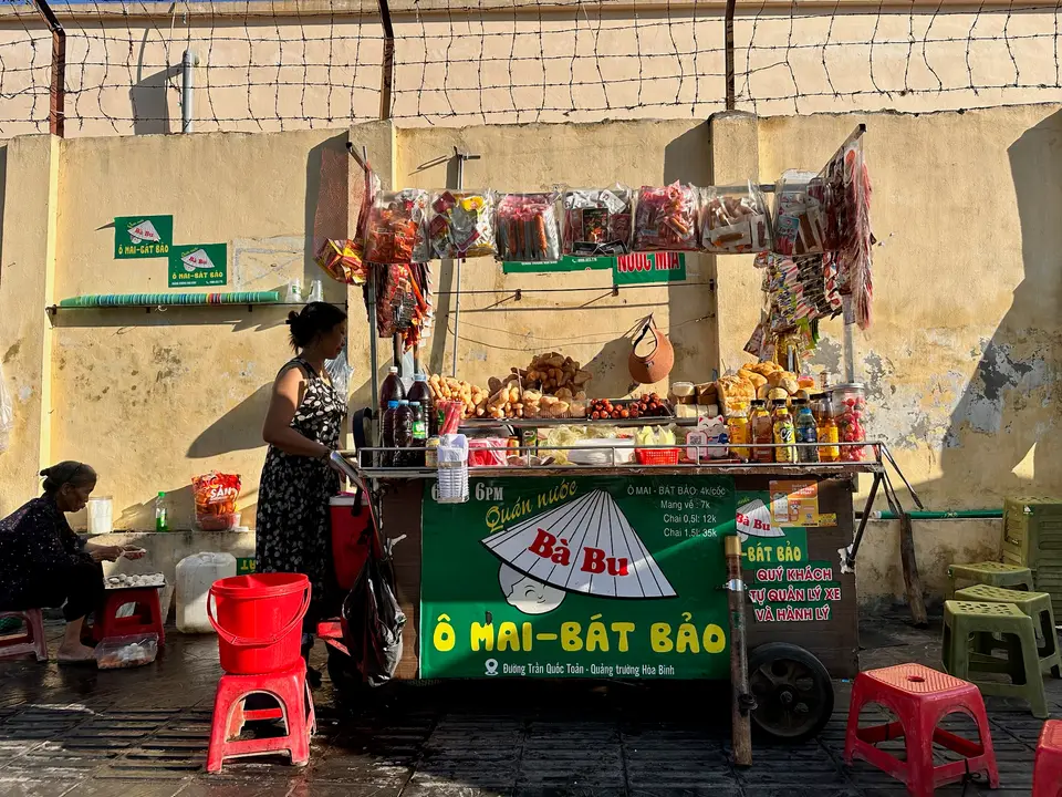 Le stand familial Bà Bu sur un trottoir du Vietnam : chariot vitré, parasol et tabourets rouges.